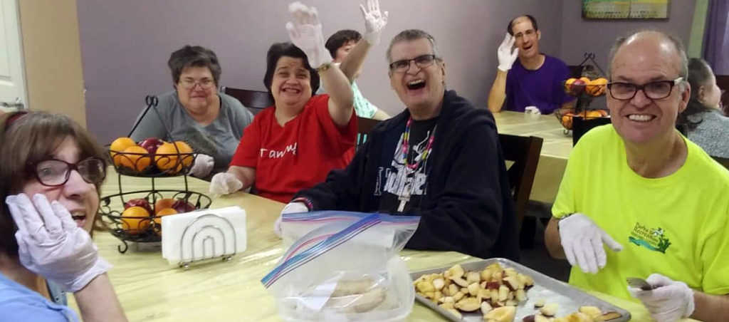 Seven residents sit around a table, all smiling and waving at the camera.