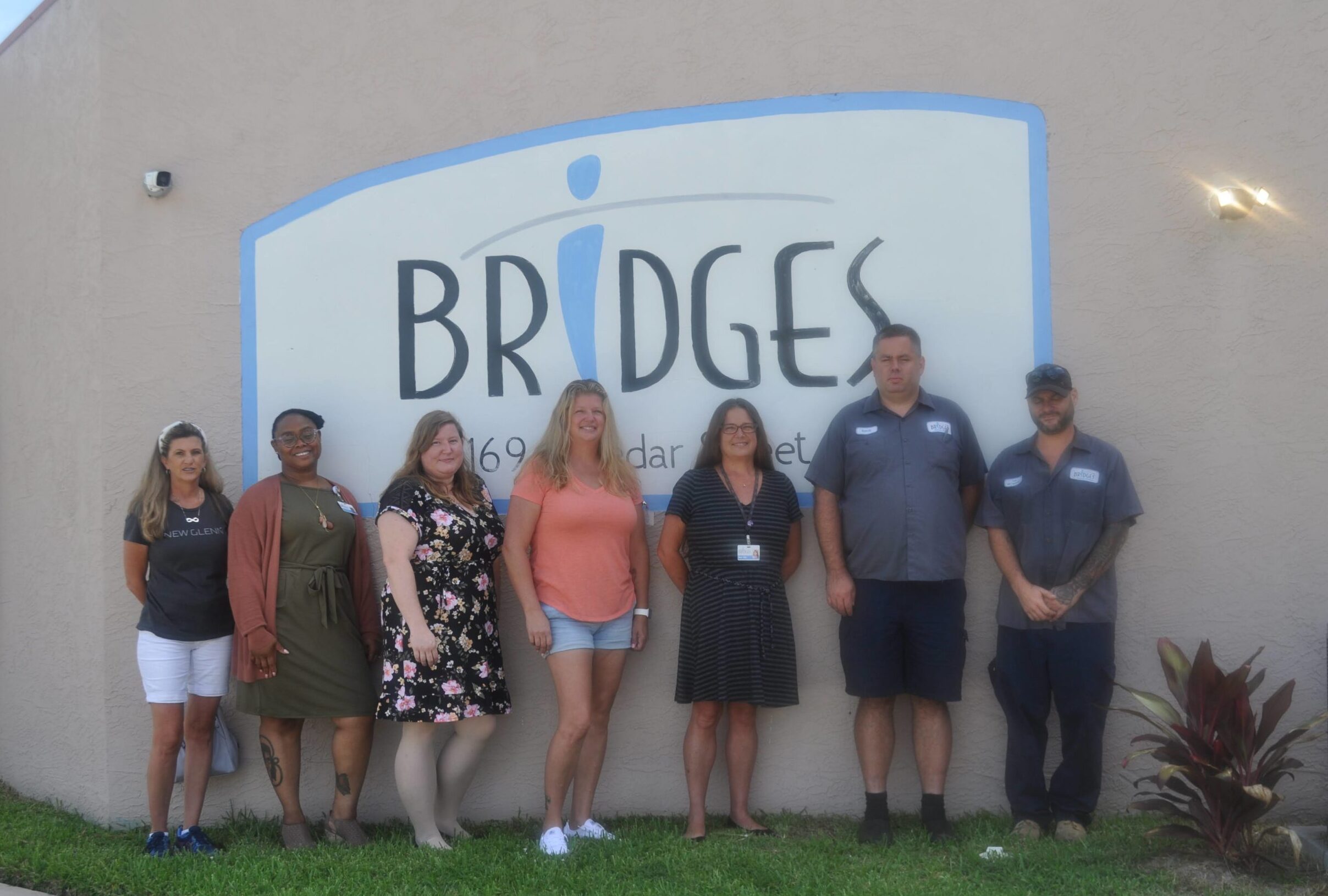 Image description: seven staff members stand in front of a wall with a large sign that has the Bridges logo.